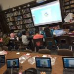 several students sitting at tables while using computers