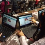 Students sitting at tables and using touchscreen chromebooks.