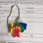 white paper form with black ink.  Beaded chain on top with six colored charms attached.