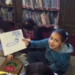 Student holding her drawing on a whiteboard of a caterpillar.
