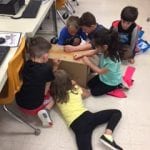 5 students sitting on floor, decorating cardboard box with crayons