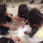 4 students sitting on floor, building a structure comprised of toothpicks and marshmallows