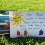 stack of books behind a sign on the lawn, reminding students to return library books