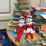two holiday elves resting on a stack of books