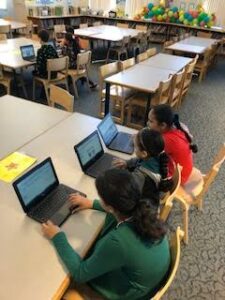 Students sitting at a large table working on a computer.