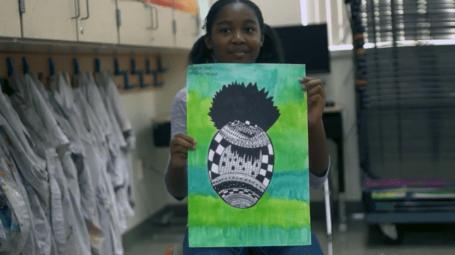A girl student is showing her black and white pineapple drawn with Zentangle techniques on a green background.