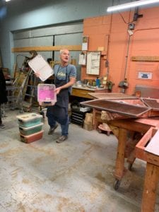 man holding a tub full of magenta pigment used to make glaze