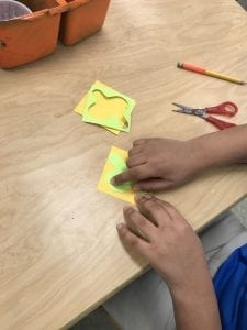 student hands arranging the shape they cut out onto a different colored square
