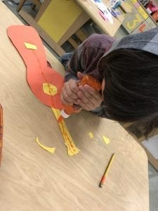Student using glitter glue to apply lines to show the strings of his paper guitar