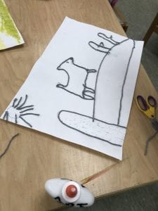 student working on a yarn painting showing an animal on a hill with a sun in the sky