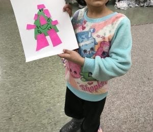 student holding artwork with a monster the shape of a triangle with rectangles for arms, legs, and hair