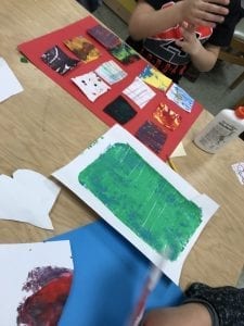 Student cutting colorful papers into rectangles and arranging them on a larger red paper