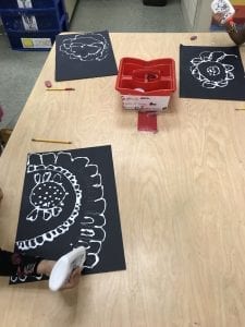 students' hands using glue bottles to draw lines of glue on top of their pencil flower drawings