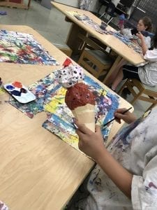 student hands holding ice cream cone sculpture and adding paint with a brush