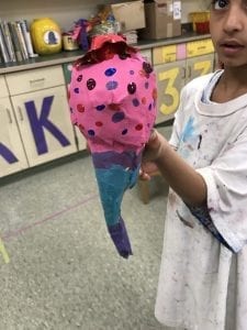 student holding an ice cream cone sculpture, it has a blue and purple cone and a pink ice cream scoop with multi-colored polka dots and a red cherry on top