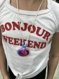 student wearing her necklace that has a colorful swirl coil in the middle and a pattern of blue and purple beads on each side of the coil