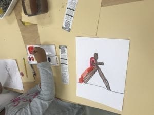 student painting with red paint around their drawing of a bubble person walking