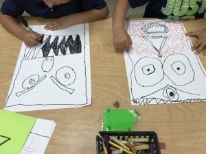 photo of students' hands drawing monsters