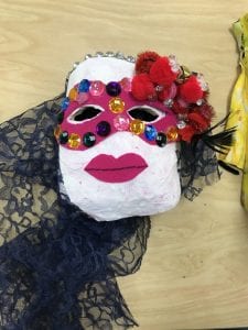 student mask that has a light pink round face, a lace veil or hair, pink lips, a pink mask that covers the eye area with jewels around the eyes