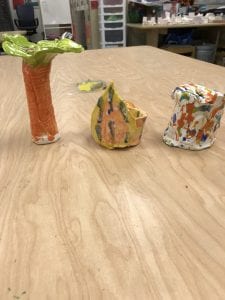 three student made ceramic pieces; one looks like a palm tree, one is a spade symbol on a bowl with splatter paint and the other is a cylinder bank with splatter paint