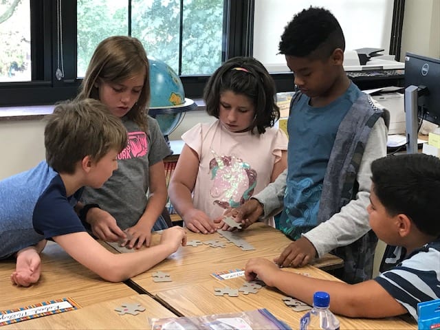 Students work puzzles picture side down in groups.