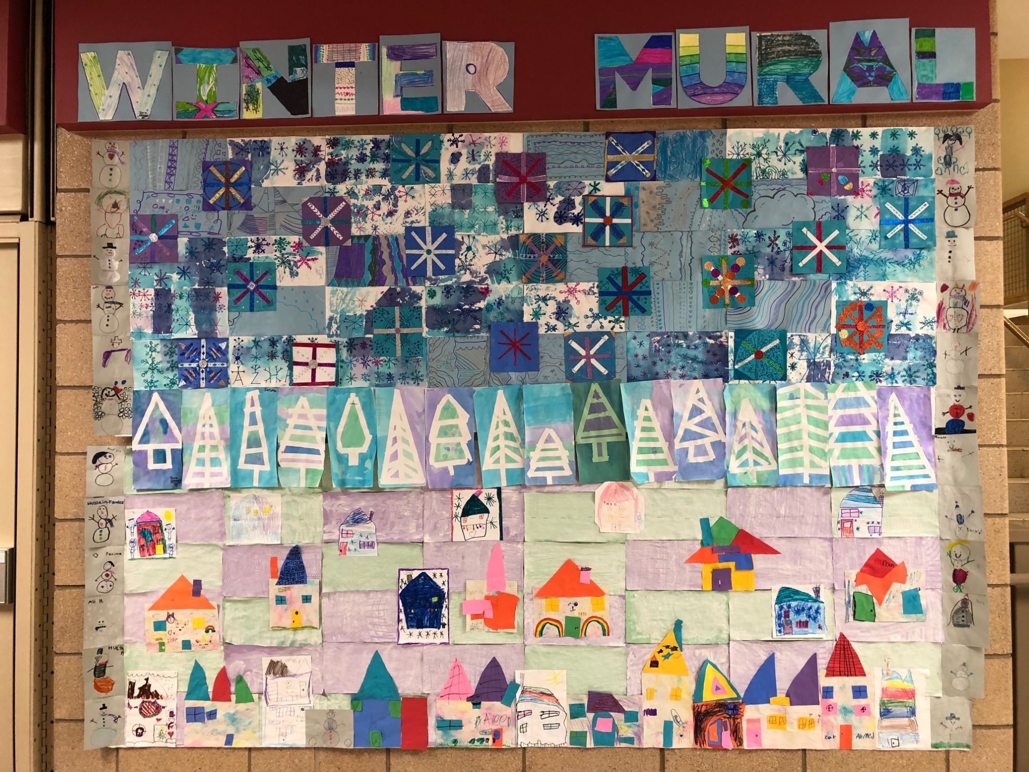 large construction paper winter mural showing snowflakes, trees, houses, and snowmen