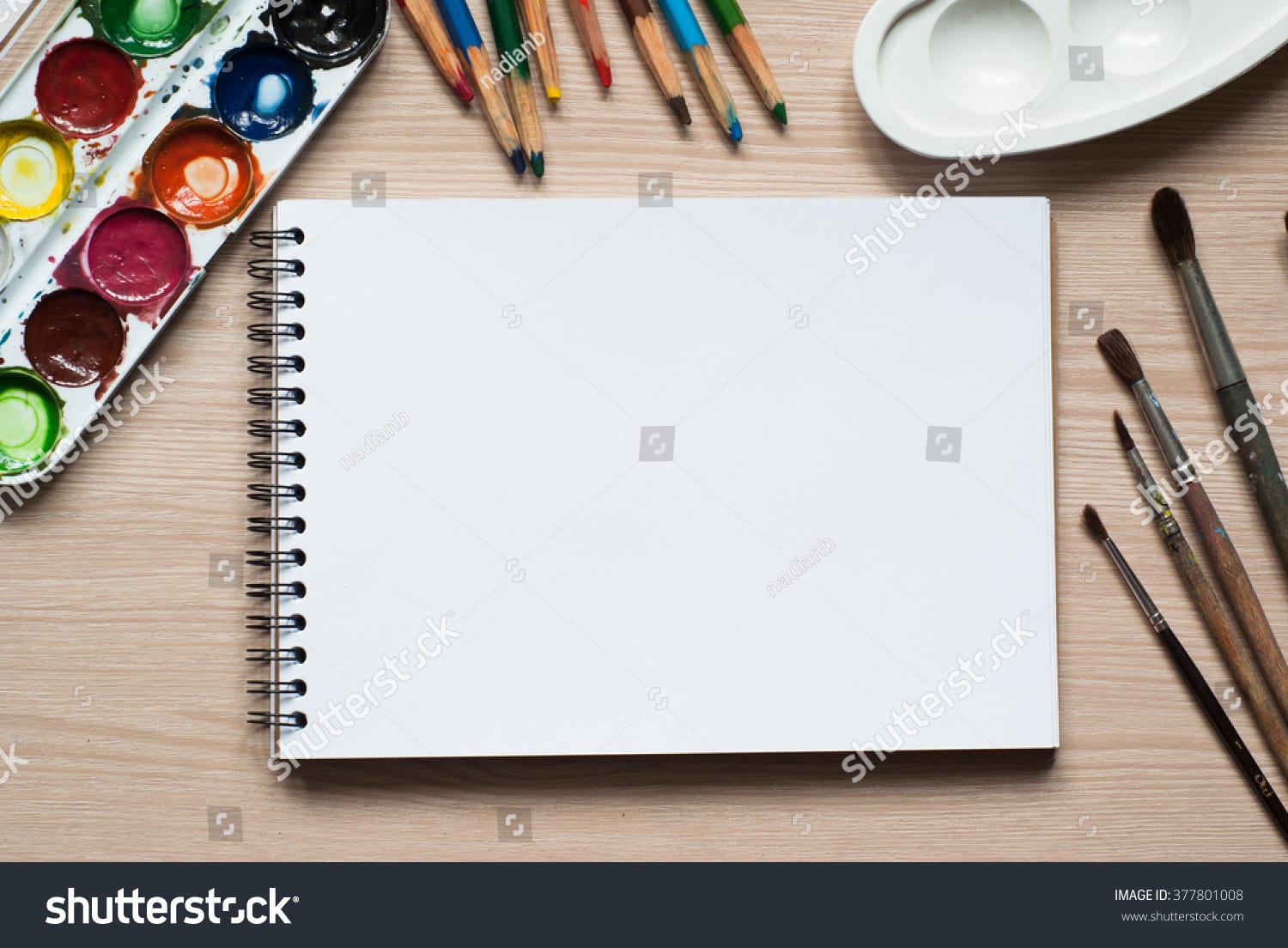 photo of open sketchpad with a paint palette and colored pencils