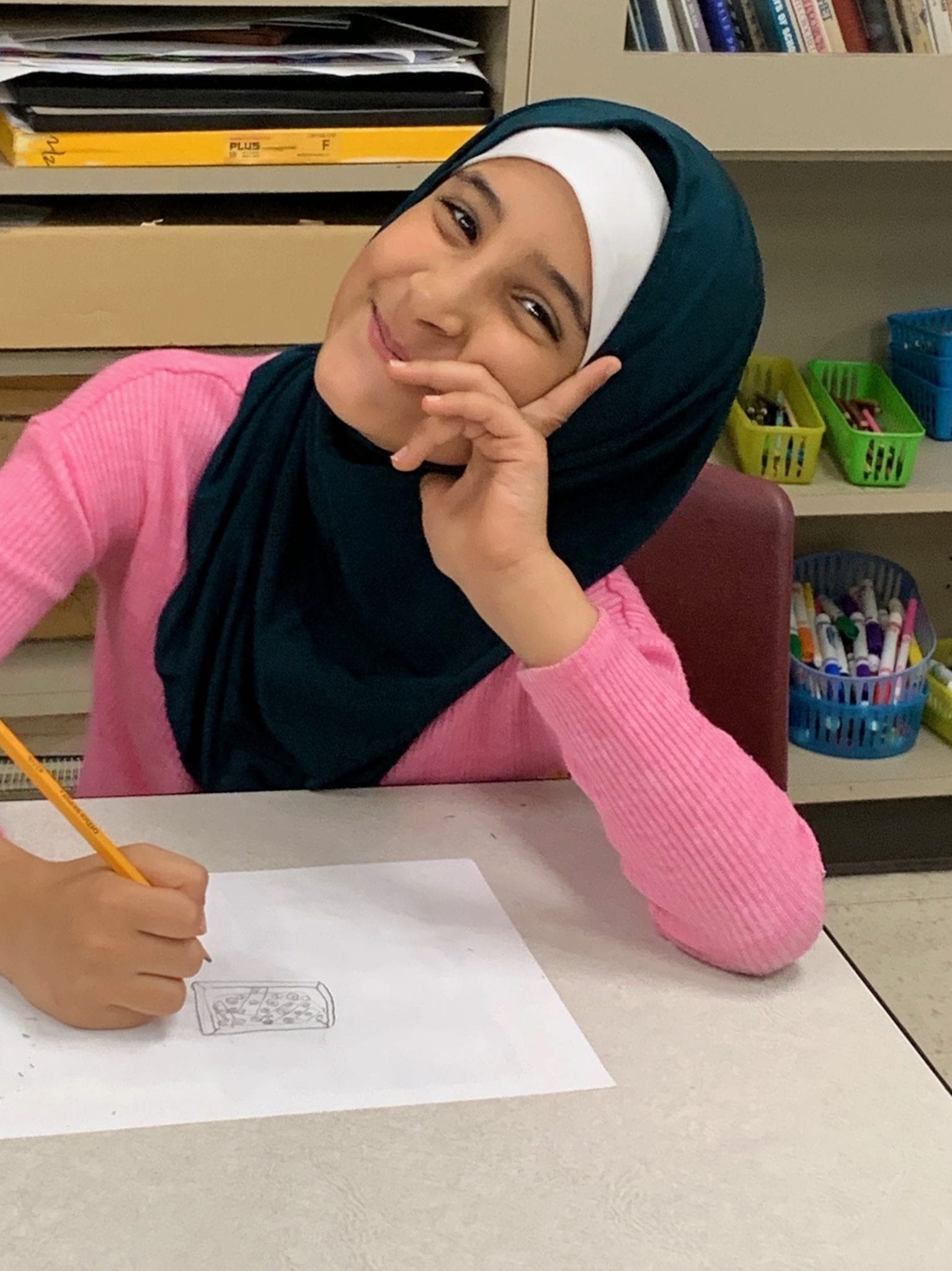 A 3rd grade girl smiles as she takes a break from drawing.