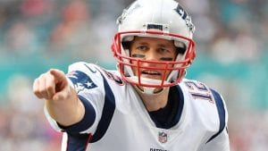 photo of Brady wearing a football helmet and a patriots jersey pointing at something past the camera