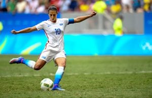 image of Lloyd wearing an American soccer jersey kicking a soccer ball with her arms stretched out wide