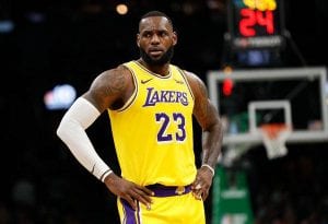 James wearing a yellow Lakers jersey, standing on a basketball court with is hands on his hips and looking to the side