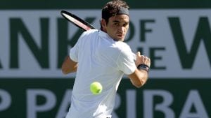 image of Federer wearing a white tennis shirt and black sweatband holding a tennis racket looking at a ball as it is coming towards him, about to swing his racket to hit it