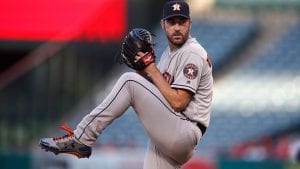 Verlander about the pitch a baseball; he has his hands in his glove with the ball, his leg is raised and he is looking in the distance