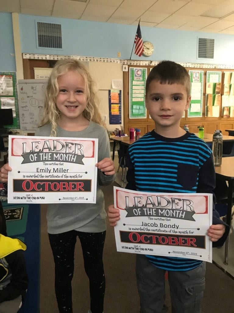 two students hold up their leader of the month certificates and smile