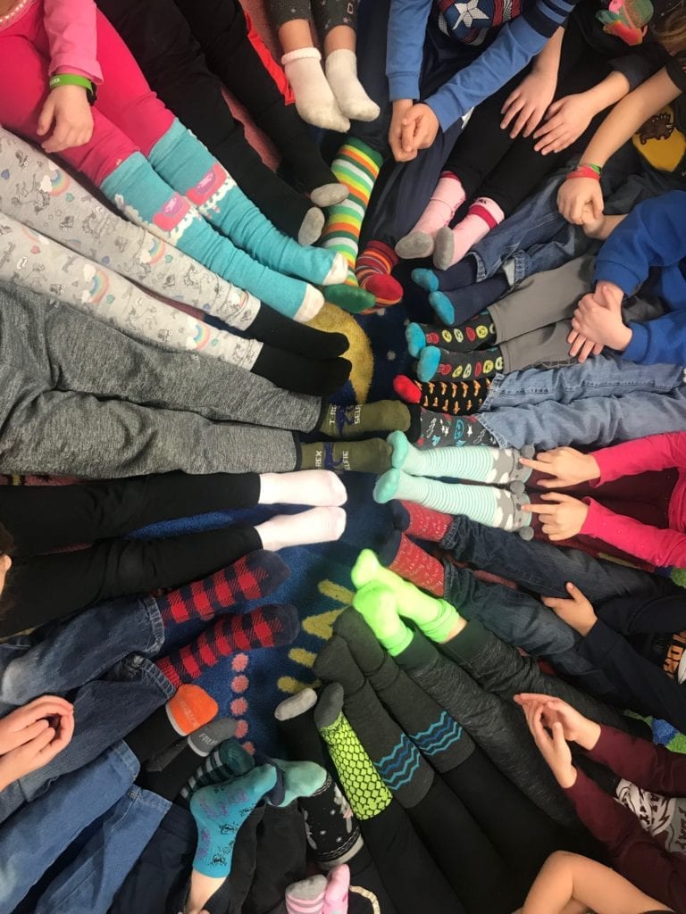 Students sit in a circle with their feet in the middle showing off their crazy socks