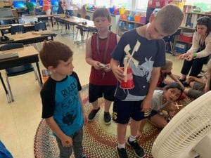 three students show off their wind turbine working