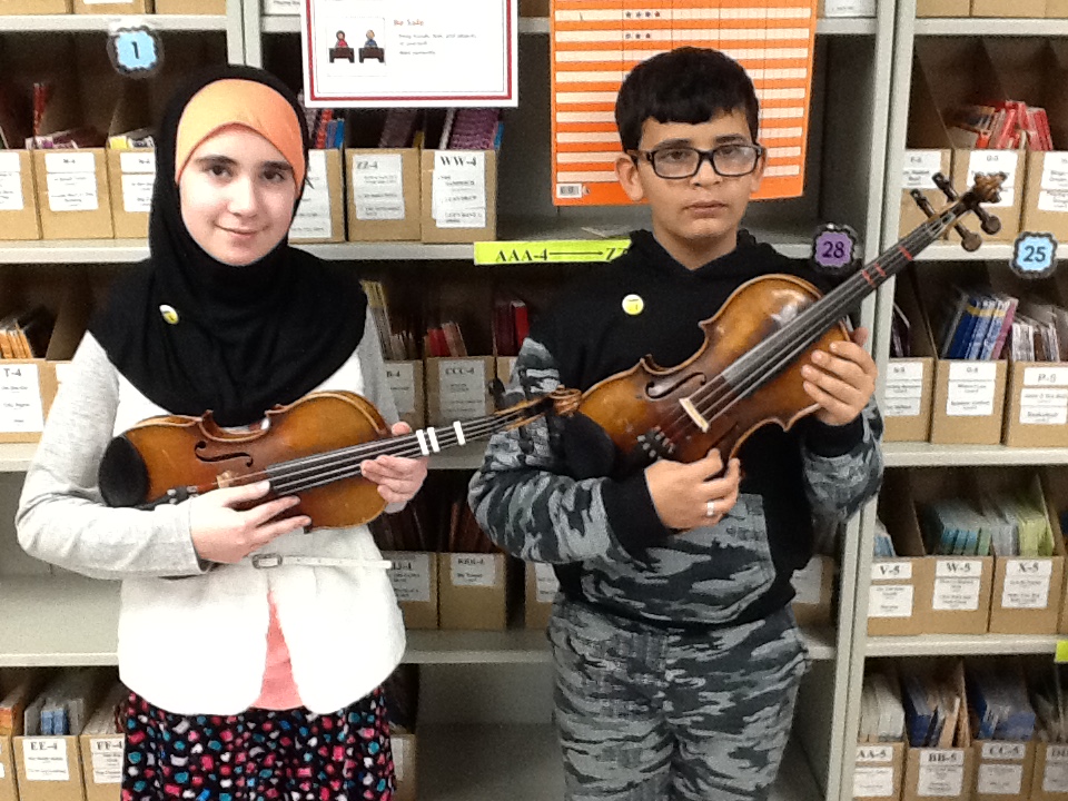 Aya and Haussen holding their violins and wearing their Cadet Pins