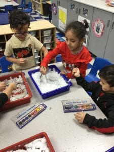 3 children using paint brushes in a tray of snow.