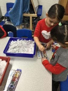 Two children dipping paint brushes into watercolor paint next to a tray of snow.