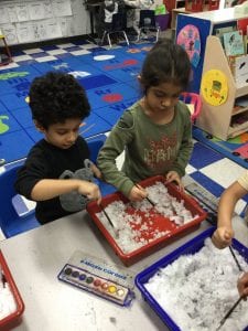 Two children using paint brushes in a tray of snow.