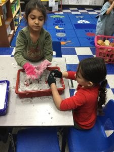 Two children wearing gloves putting their hands into a tray of snow.
