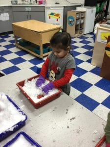 A child, wearing gloves, putting hands into a tray of snow.