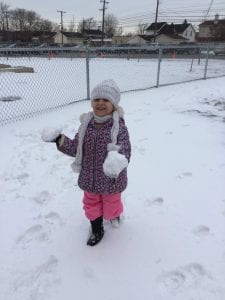 Girl walking outside carrying snowballs in each hand.