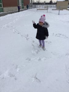 A girl outside holding up a snowball.
