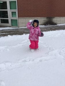A girl outside holding up a snowball.