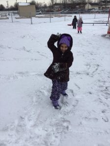A girl standing outside holding a snowball.
