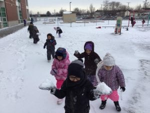 Boys and girls outside holding snow in their hands.